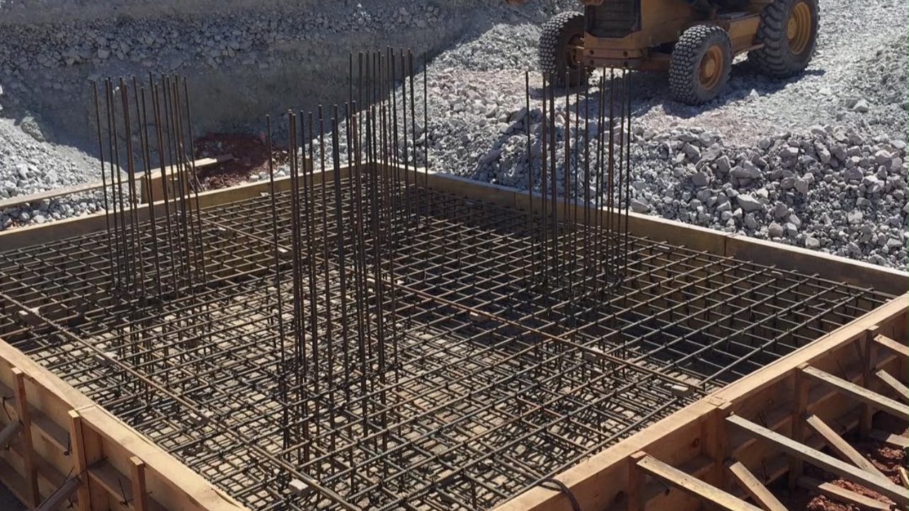Armado y cimbra de una cimentación revisados en campo, con retroexcavadora al fondo